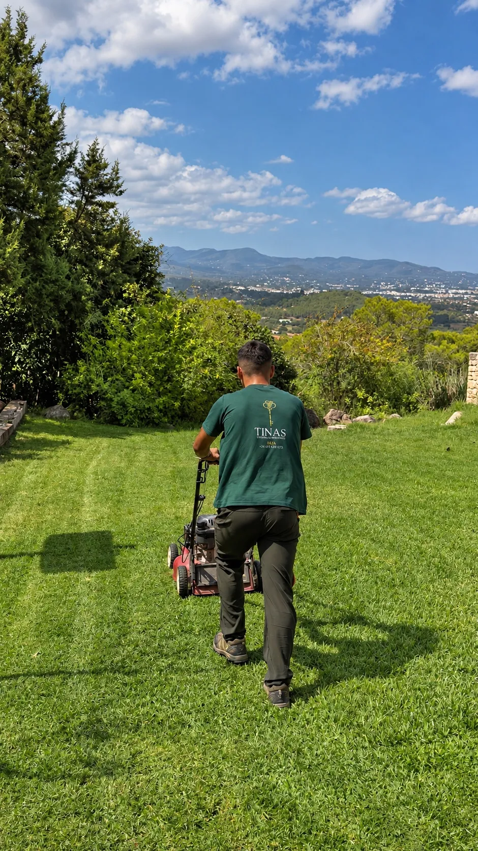 TINAS team member mowing a villa lawn with the hills of Ibiza in the background